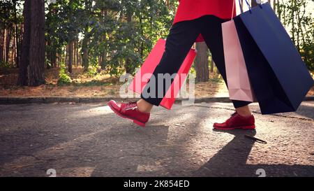 femme avec sacs de shopping. jambes de femme en chaussures rouges, gros plan. Femme avec des sacs de shopping colorés dans ses mains, marchant dans le parc de la ville. Shopping et cadeaux. Livraison ou don concept. Photo de haute qualité Banque D'Images