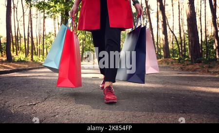 femme avec sacs de shopping. jambes de femme en chaussures rouges, gros plan. Femme avec des sacs de shopping colorés dans ses mains, marchant dans le parc de la ville. Shopping et cadeaux. Livraison ou don concept. Photo de haute qualité Banque D'Images