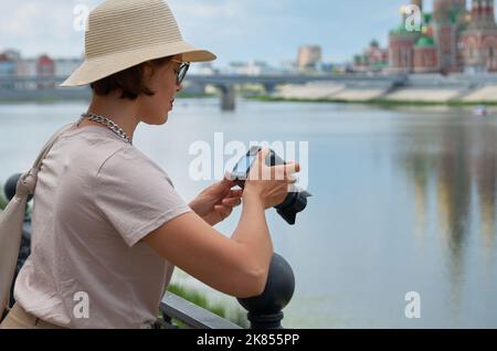 Femme touriste dans un chapeau de paille prend des photos dans la rue avec un appareil photo d'époque Banque D'Images