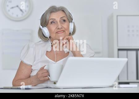 Femme âgée dans un casque suivre un cours en ligne sur ordinateur à la maison. Banque D'Images