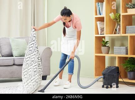 Je ne balaie pas les choses sous le tapis, je m'occupe du désordre. Une jeune femme passant l'aspirateur dans la salle de séjour. Banque D'Images