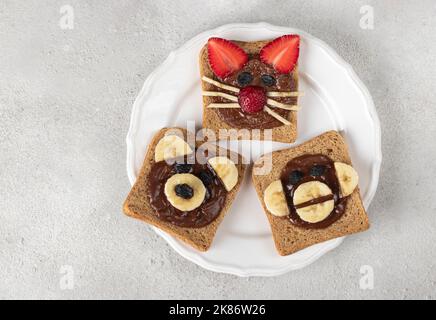 Trois toasts doux pour les enfants en forme de chat, d'ours et de singe, avec fraises, banane, fromage à la crème et chocolat, vue du dessus Banque D'Images