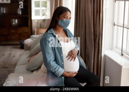 La grossesse a été une expérience difficile pendant la pandémie. Une femme enceinte portant un masque facial et regardant à la maison. Banque D'Images
