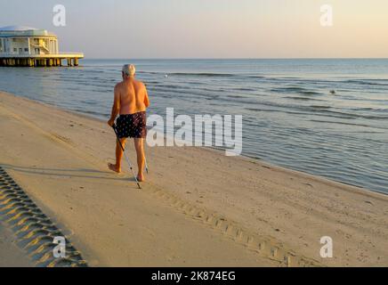 Juillet 2022 Senigallia, Italie: Homme aîné marchant avec un bâton vers Rotonda al mare sur la plage à travers la mer, le ciel de lever du soleil, et l'horizon Banque D'Images