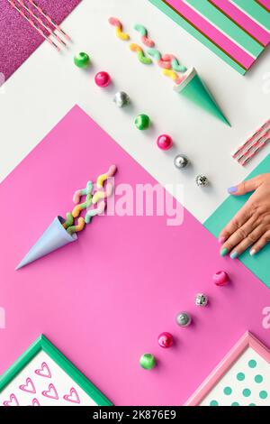 Tasses à café, chocolat, bonbons et tourbillon de lollipop arc-en-ciel. Tasses en céramique et main humaine avec ongles manucurés. Arrière-plan à couches géométriques en gras Banque D'Images