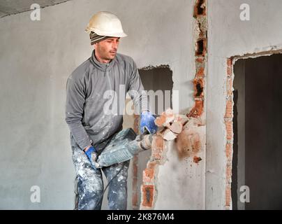 Travailleur dans un casque de protection avec perforateur achèvement de la déconstruction du reste du mur de briques à l'intérieur de la pièce. Le constructeur fait des travaux de réparation sur le démontage des murs et des cloisons. Banque D'Images