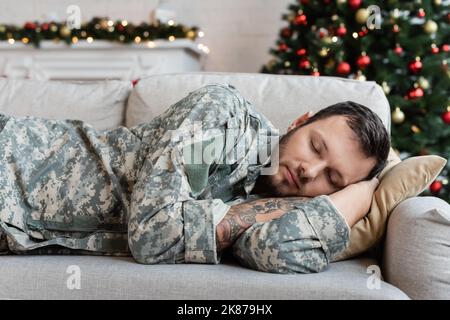 homme barbu fatigué en uniforme militaire dormant sur un canapé à la maison le jour de noël Banque D'Images