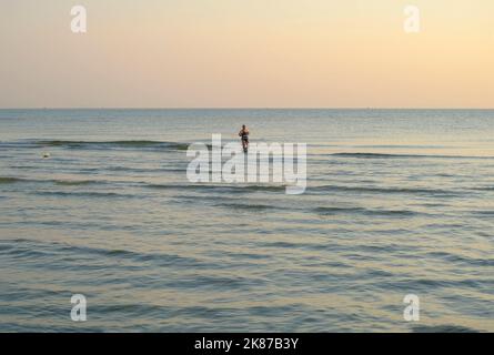 Juillet 2022 Senigallia, Italie: Femme aînée marchant dans la mer sur le coucher du soleil acros l'horizon. Banque D'Images