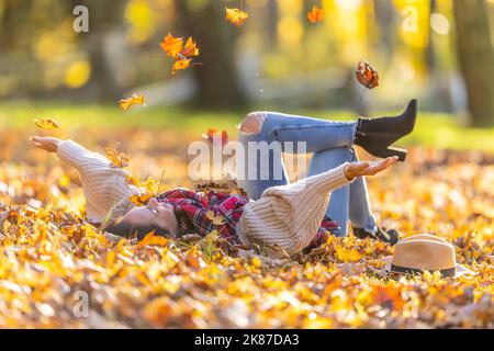 Une belle brunette insouciante, située dans le parc, jette des feuilles mortes pendant le coucher de soleil d'automne. Banque D'Images