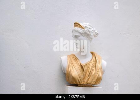 Buste antique de tête de femme contre le mur gris. Statue historique en robe dorée. Visage de femme antique sur fond clair. Photo de haute qualité Banque D'Images