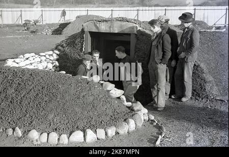 1938, travailleurs gallois historiques à l'entrée d'un abri de raid aérien récemment construit dans le domaine industriel de Treforest, à Rhondda, au sud du pays de Galles. Aussi connu sous le nom d'Anderson refuges, après le ministre de la sécurité intérieure de l'époque, Sir John Anderson, ils étaient une forme de protection contre les raids aériens en WW2, étant des structures en acier enterrées à mi-chemin dans le sol et recouvertes d'une couche de terre épaisse. Leur construction a commencé en 1938 comme une mesure préventive alors que la guerre était à l'horizon et que les attaques aériennes étaient inévitables. Au moment où la guerre a été déclarée en septembre 1939, quelque 1,5 millions d'abris avaient été construits. Banque D'Images