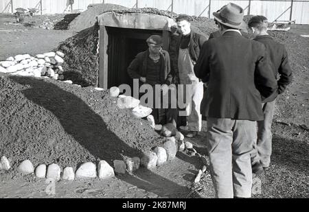 1938. Travailleurs gallois historiques à l'entrée d'un abri de raid aérien récemment construit au domaine industriel de Treforest, à Rhondda, au sud du pays de Galles. Aussi connu sous le nom d'Anderson refuges, après le ministre de la sécurité intérieure de l'époque, Sir John Anderson, ils étaient une forme de protection contre les raids aériens en WW2, étant des structures en acier enterrées à mi-chemin dans le sol et recouvertes d'une couche de terre épaisse. Leur construction a commencé en 1938 comme une mesure préventive alors que la guerre était à l'horizon et que les attaques aériennes étaient inévitables, au moment où la guerre a été déclarée en septembre 1939, quelque 1,5 millions d'abris avaient été construits. Banque D'Images