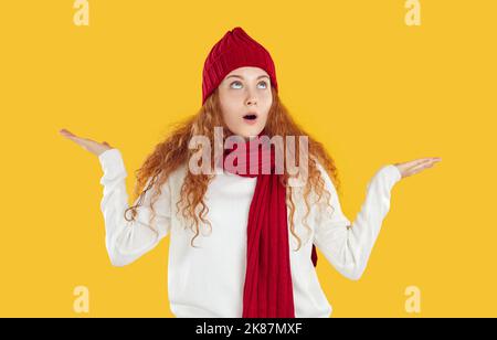 Drôle jeune femme en chapeau chaud et foulard tend à attraper des flocons de neige tout en regardant vers le haut dans la surprise. Banque D'Images