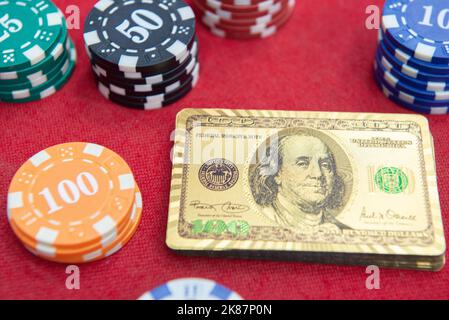 Vue de dessus des cartes à jouer dorées de 100 dollars à côté des piles de jetons sur la table en feutre rouge. Le jeu de poker est l'un des jeux de cartes les plus populaires dans le monde a Banque D'Images