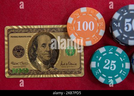 Vue de dessus des cartes à jouer dorées de 100 dollars à côté des piles de jetons sur la table en feutre rouge. Le jeu de poker est l'un des jeux de cartes les plus populaires dans le monde a Banque D'Images