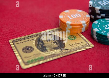 Vue de dessus des cartes à jouer dorées de 100 dollars à côté des piles de jetons sur la table en feutre rouge. Le jeu de poker est l'un des jeux de cartes les plus populaires dans le monde a Banque D'Images