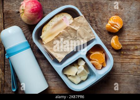 boîte à lunch pour écoliers avec thermos sur fond de bois. pomme, mandarine, sandwich dans la boîte à lunch et bouteille d'eau Banque D'Images