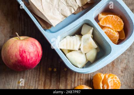 boîte à lunch pour écoliers sur fond de bois. pomme, mandarine, sandwich dans la boîte à lunch Banque D'Images