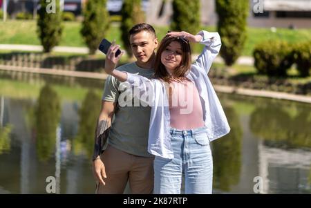 Image d'un jeune heureux beau couple aimant posant à l'extérieur dans la nature du parc prendre selfie par téléphone mobile Banque D'Images