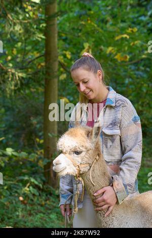 Un Sunbeam rencontre une jeune femme avec beige Alpaca sur Forest Path. Dans la Forêt verte de fond. Bauma, Oberland de Zurich, Suisse Banque D'Images