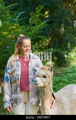 Un Sunbeam rencontre une jeune femme avec beige Alpaca sur Forest Path. Dans la Forêt verte de fond. Bauma, Oberland de Zurich, Suisse Banque D'Images