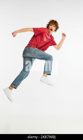 Portrait complet d'un jeune homme excité qui court, danse, s'amusant isolé sur fond blanc. Sport, danse, fitness, bonheur Banque D'Images