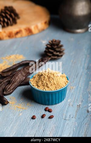 Gousses de caroube et poudre de caroube sur fond bleu en bois. Banque D'Images