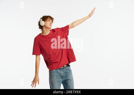 Jeune homme rêvant, étudiant en t-shirt rouge et casque isolé sur fond blanc. Concept des émotions, expression faciale, jeunesse, musique Banque D'Images