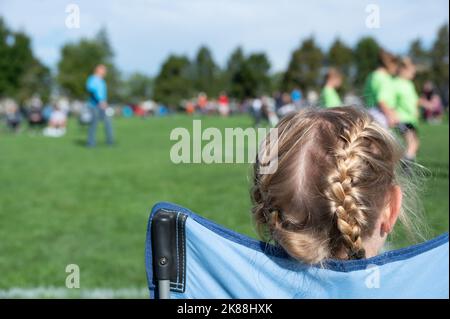 Une jeune sœur regarde un match de football pour soutenir son frère. Banque D'Images