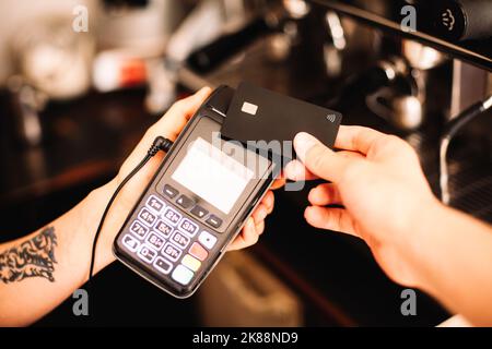 Le barista tient le terminal du lecteur de carte de crédit pendant que le client effectue un paiement sans contact à l'aide d'une carte de crédit Banque D'Images