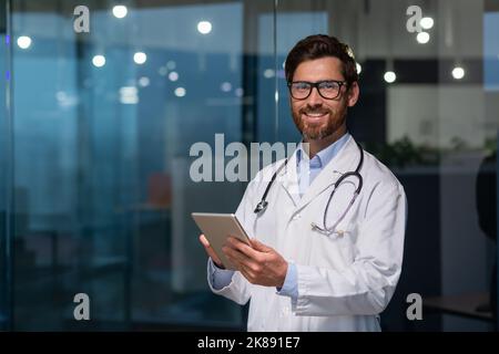Portrait d'un médecin mature et expérimenté, d'un homme en manteau médical et de lunettes regardant la caméra, doc utilisant un ordinateur tablette, travaillant dans une clinique de bureau moderne Banque D'Images