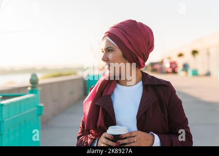 Jeune arabe musulmane dans hijab marchant sur le front de mer de la rue et buvant du café à emporter Banque D'Images