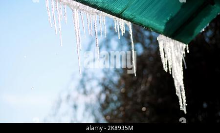 hiver, givré, enneigé, ensoleillé jour. gros plan, de grandes glaces transparentes pendent du toit, contre le ciel. Photo de haute qualité Banque D'Images