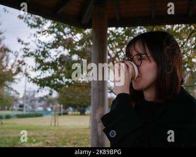 Une belle dame japonaise qui boit du café dans un parc Banque D'Images