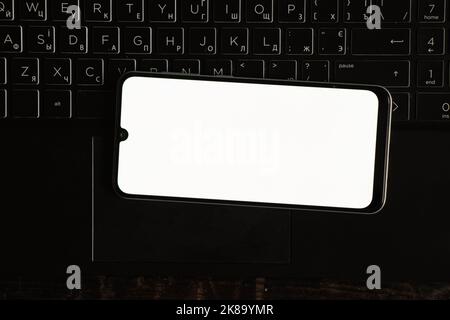 un téléphone avec écran blanc se trouve sur un ordinateur portable noir sur une table, un modèle de téléphone avec écran blanc Banque D'Images