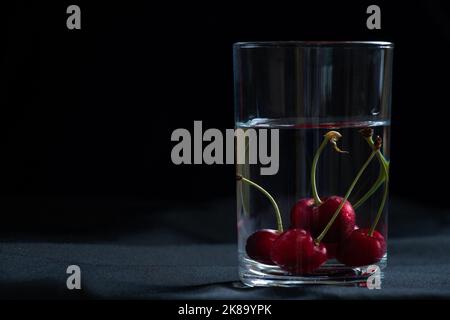 cerises dans un verre d'eau sur fond noir sur la table, fond de fruits, fruits Banque D'Images