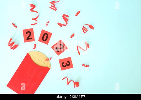 2023 concept chinois de célébration de la nouvelle année. Composition de couche plate d'enveloppe rouge avec confettis. Banque D'Images