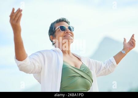 Maintenant c'est la liberté que j'avais à l'esprit. Une femme mûre attrayante debout dehors seul et levant ses mains pendant une journée sur la plage. Banque D'Images