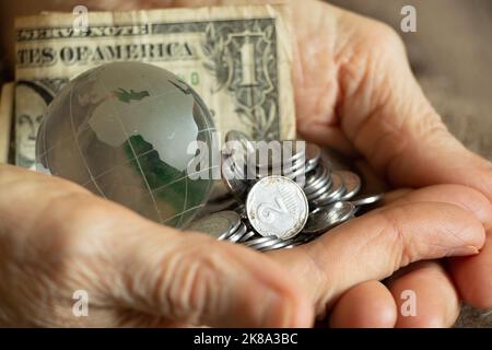 Les dollars américains et les centimes ukrainiens et un globe de verre de la planète se trouvent entre les mains d'une vieille femme, de la finance et du peuple Banque D'Images