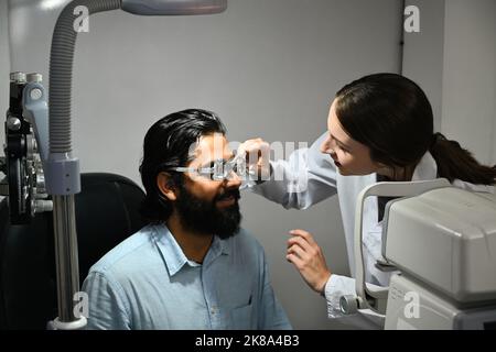 Optométriste effectuant des tests de vue pour un patient mâle avec des lunettes ophtalmiques spéciales en clinique. Contrôle de la santé oculaire et concept d'ophtalmologie Banque D'Images