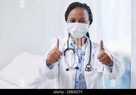 Elle est pour la promotion de la santé et la prévention des maladies. Portrait d'un jeune médecin portant un masque facial et montrant les pouces vers le haut dans un hôpital. Banque D'Images