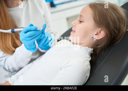 Un dentiste pédiatrique parle de la procédure de polissage des dents à une petite fille souriante Banque D'Images