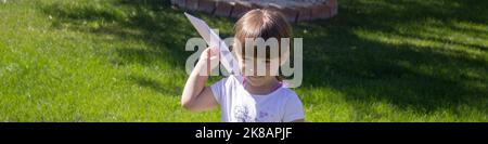 Adorable petite fille jouant pour voler un avion en papier dans le jardin à la maison. Jeux en plein air. Bannière horizontale Banque D'Images