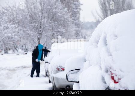 Voitures garées dans la neige le matin après un blizzard, le conducteur nettoie la neige de sa voiture, Ukraine Dnipro Banque D'Images