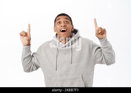 Portrait d'un gars afro-américain excité pointant du doigt vers le haut, affiche la publicité sur le dessus, texte promotionnel, se dresse sur fond blanc Banque D'Images