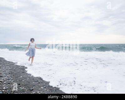 Une femme heureuse est en train de courir sur les vagues de la mer de tempête. Femme aux cheveux rouffés avec le vent. Concept Wanderlust. Vacances sur la côte de mer. Banque D'Images