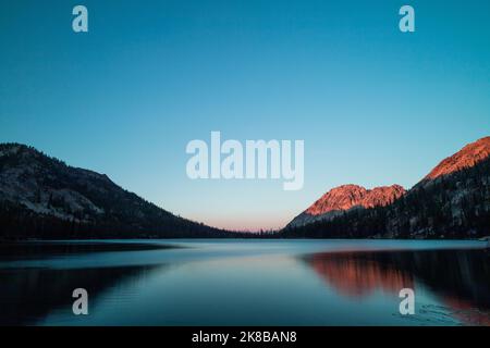 Le lac Toxaway, situé dans la région sauvage de Sawtooth dans l’Idaho, vu en soirée d’été au coucher du soleil, avec une crête de montagne illuminée de rayons rouges du soleil. Banque D'Images