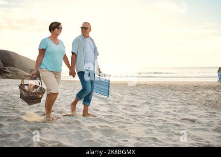 Prêt pour une journée de détente à la plage. Un couple à la plage avec un panier de pique-nique et des chaises. Banque D'Images