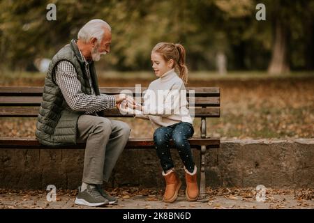 Beau grand-père jouant les mains rouges jeu de claquement avec sa petite-fille dans le parc le jour de l'automne Banque D'Images