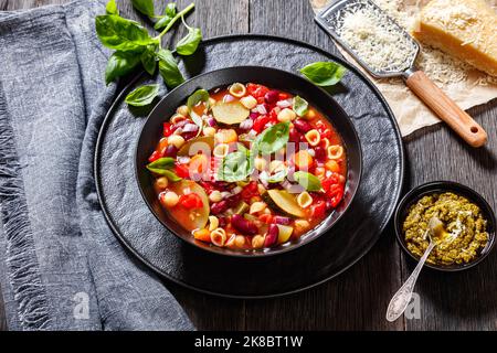 soupe minestrone aux haricots rouges, courgettes, haricots garbanzo, petites pâtes, fromage, tomates, carottes et basilic dans un bol noir Banque D'Images